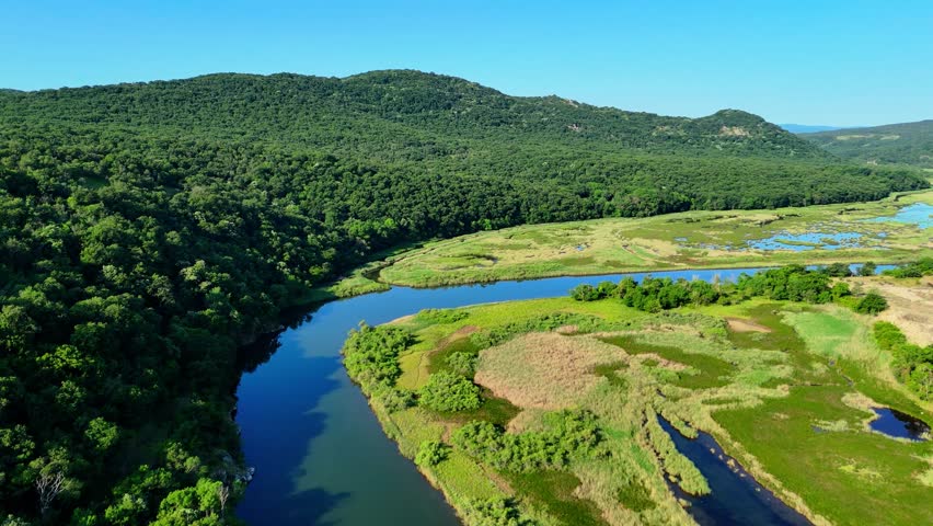 Stunning 4K drone footage showing the estuary of the Ropotamo River where it meets the Black Sea, captured from high above. The video features the river winding through lush marshlands and wetland are