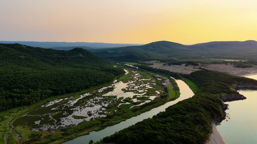 Stunning 4K drone footage showing the estuary of the Ropotamo River where it meets the Black Sea, captured from high above. The video features the river winding through lush marshlands and wetland are