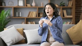 Allergic young woman sneezes and wipes her nose with handkerchief. Unhealthy adult female suffering from seasonal allergies sitting on sofa in living room at home. Girl is sick with cold, virus or flu - Powered by Shutterstock - Get 15% off with code: PIKWIZARD15
