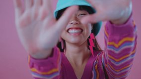 Trendy asian woman radiating confidence, wearing turquoise bucket hat and pink lightning bolt earrings, smiling warmly against vibrant pink studio backdrop with stylish, carefree pose - Powered by Shutterstock - Get 15% off with code: PIKWIZARD15