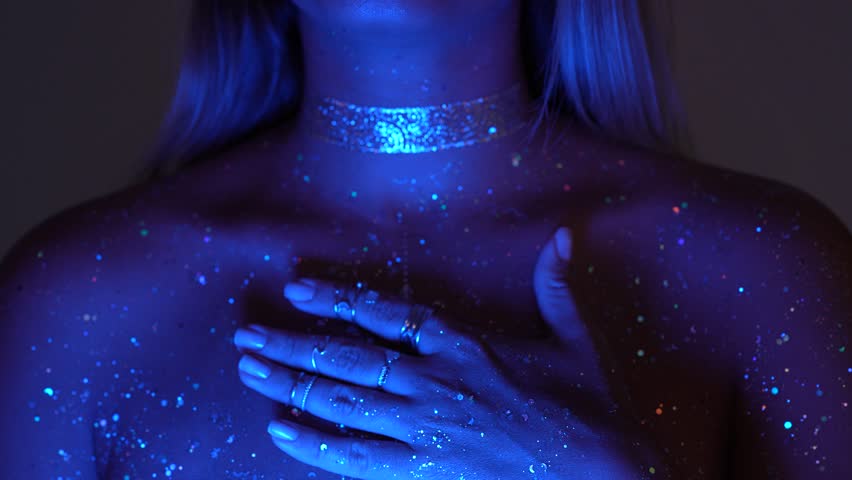 A young mesmerising cosmic woman breathes deeply with her hand on chest. The light glows from within, like a star remembering itself. Her alien soul radiates through silence and shimmer
