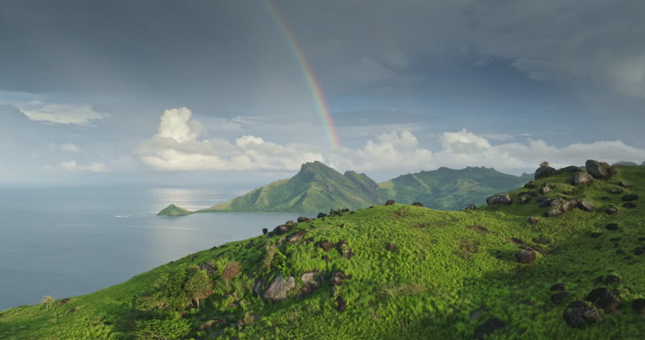 Stunning aerial view of a vibrant rainbow arching over lush green mountains and tranquil blue water ocean bay, creating a picturesque tropical island landscape. Amazing nature travel background