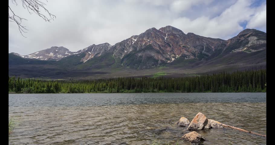 Breathtaking aerial view of towering Rocky Mountains, emerald lake, and blue sky in Canada. People biking along a scenic path between the lake and mountains. Majestic landscape, high mountains,