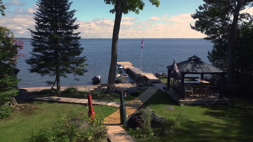 A boardwalk leading to a dock on a lake with a Canadian flag and a gazebo. During a sunny day at a summer cottage.