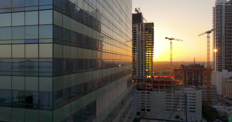 Aerial view of new developing residence in American urban area at sunset. Tower cranes at industrial construction site in Miami, Florida. Concept of housing growth in the USA.