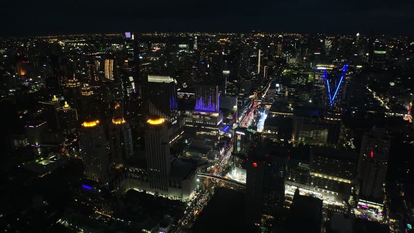 BANGKOK, THAILAND - AUGUST 2024 : Aerial high angle view of Bangkok city. View of buildings and streets around downtown Siam area at night.