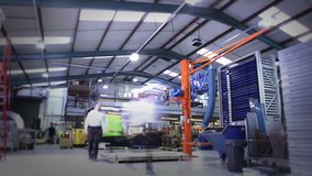 Time-lapse clip of busy workers in a warehouse or factory, wearing high visibility clothing and hard hats. They are checking stock levels and using a forklift truck to move empty wooden pallets.