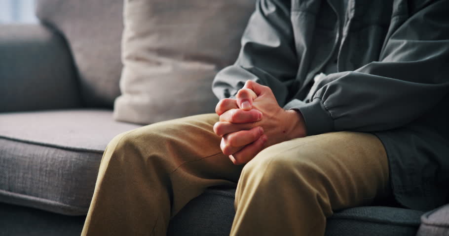 Hands, nervous or man on sofa with anxiety for trauma, mental health or overthinking with stimming. Worry, person with depression and fidget in home with stress, overwhelmed or panic attack in lounge
