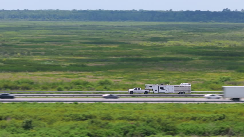 Truck towing RV camper trailer with horse equine carrier driving at high speed on American freeway in Florida. USA travel transportation infrastructure.