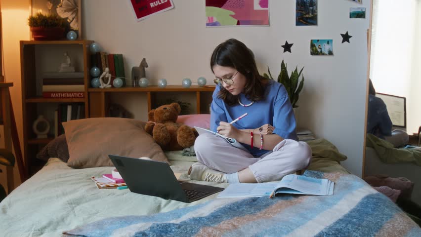 Teenage girl with prosthetic arm writing in her notebook and reading book while doing her homework on bed in her cozy room - Powered by Shutterstock - Get 15% off with code: PIKWIZARD15