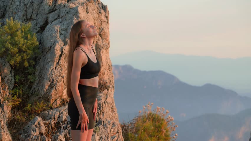 Young fit woman in sportswear doing shoulder warm-up outdoors at sunset in summer. Light smile on her face. Stretching before evening workout. Concept of mobility, balance, and wellbeing.