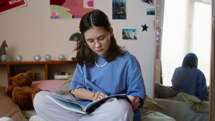 Dedicated teenager girl with glasses and prosthetic arm reading book on her bed in her colorful room - Powered by Shutterstock - Get 15% off with code: PIKWIZARD15