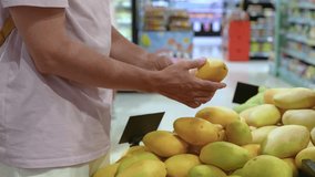 Unrecognizable man examing mango fruit, squeezing to test ripeness before buy. Fresh tropical fruit selection, grocery shopping, travel destination in grocery market, local produce quality checked - Powered by Shutterstock - Get 15% off with code: PIKWIZARD15