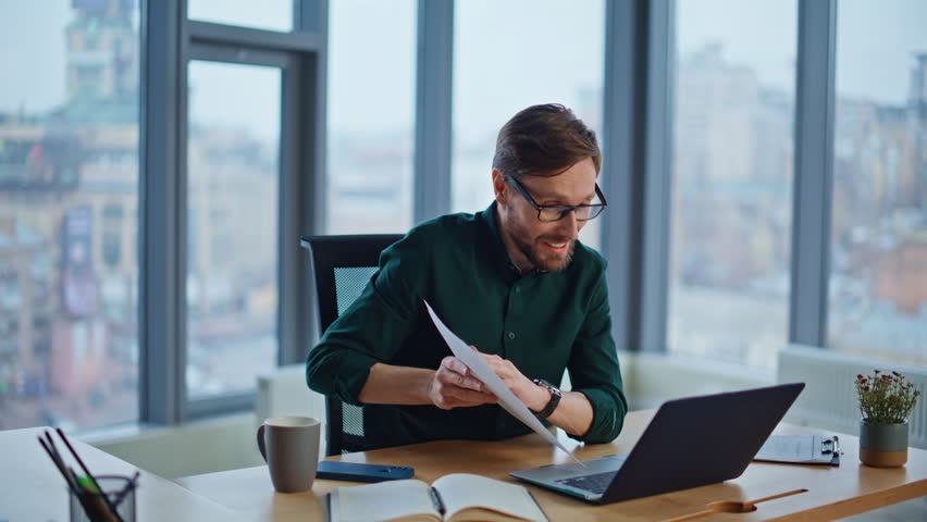 Smiling manager consulting at video conference showing papers to laptop webcam in modern office closeup. Professional businessman in glasses talking at online call. Happy employee have virtual meeting - Powered by Shutterstock - Get 15% off with code: PIKWIZARD15