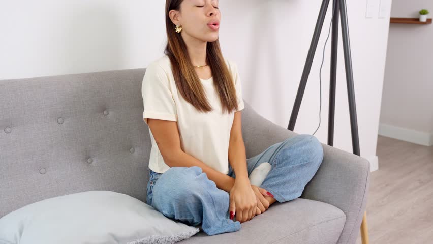 Neurodivergent young woman practicing a breathing exercise while sitting on a sofa, promoting mindfulness and self regulation