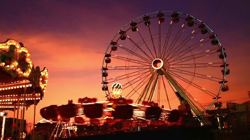 Illuminated Ferris Wheel and Amusement Park Rides at Sunset