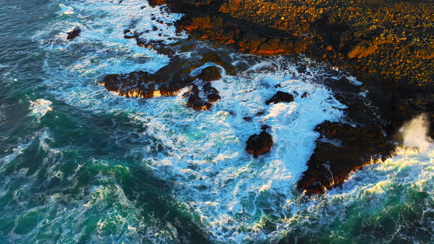 Top down view on ocean waves crashing and foaming around majestic rocks and cliffs. Inspiring and incredible nature concept. Drone shot of powerful sea water on epic coastline in Iceland