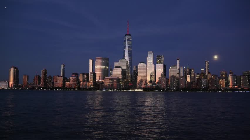 nyc skyline view of downtown manhattan skyscrapers at sunset dusk blue hour (glow glowing reflection from buildings) moving water flowing hudson river moonrise moon shining last light buildings nj