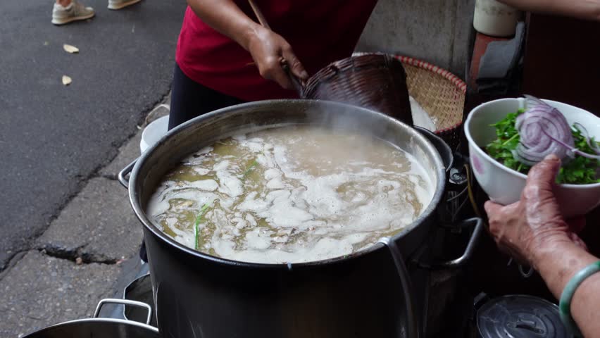 Steaming broth being prepared at a bustling street food stall in Hanoi, Vietnam during the morning hours