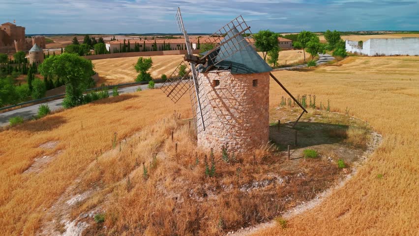 Aerial view of an old windmill with the historic Castle of Belmonte in the background, Cuenca Province, Spain. Iconic windmill from Don Quixote era standing in a scenic rural landscape.