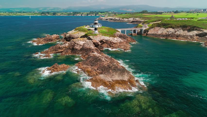 Aerial view of Faro de Ribadeo lighthouse in Lugo, Galicia, Spain. Scenic lighthouse on a rocky island on the Cantabrian Sea coast on a sunny summer day.
