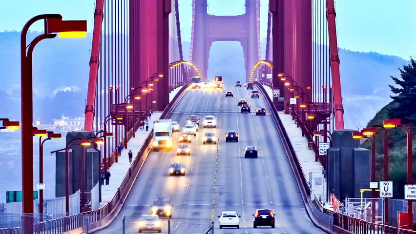 Traffic flows over Golden Gate Bridge during twilight. Vibrant red structures contrast with serene bay waters. A key landmark in San Francisco, attracting tourists and enhancing city skyline.