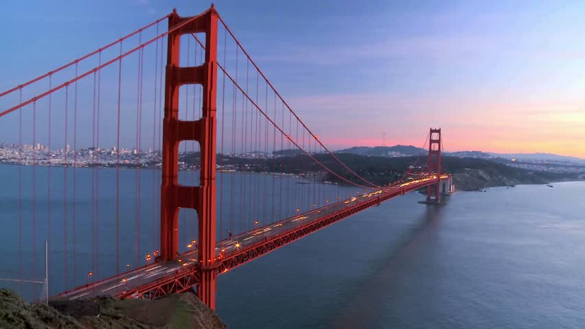 Golden Gate Bridge stands tall as dusk settles over San Francisco. Warm lights illuminate structure, while city skyline sparkles in evening glow. Ideal backdrop for travel enthusiasts and tourists.