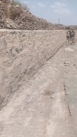 English:
This video shows a flood protection wall built along a river. On one side, a cement wall has been constructed, while the other side is reinforced with stones. The minimal use of cement indica