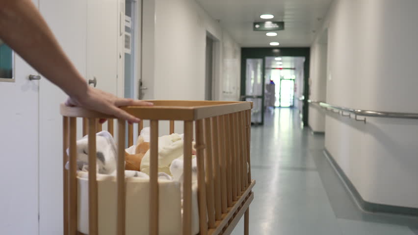 Hand pushing a crib with a newborn baby down a hospital corridor, illustrating the first week of newborn care, ideal for family, parenting, and healthcare