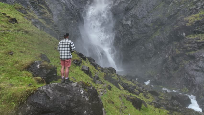 An ascending drone footage of a man standing on a rock overlooking the scenic Mardalsfossen waterfall in Molde, More og Romsdal county, Norway