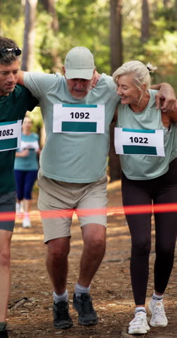 Senior man, help and trail running at finish line with woman, injury and happy for achievement in forest. People, support and muscle strain for race, team and fitness with sports challenge in woods