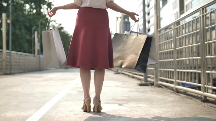 woman walking happily in street with some eco shopping bags Back view Slow motion shopping bags walking along city street Close-up beautiful woman