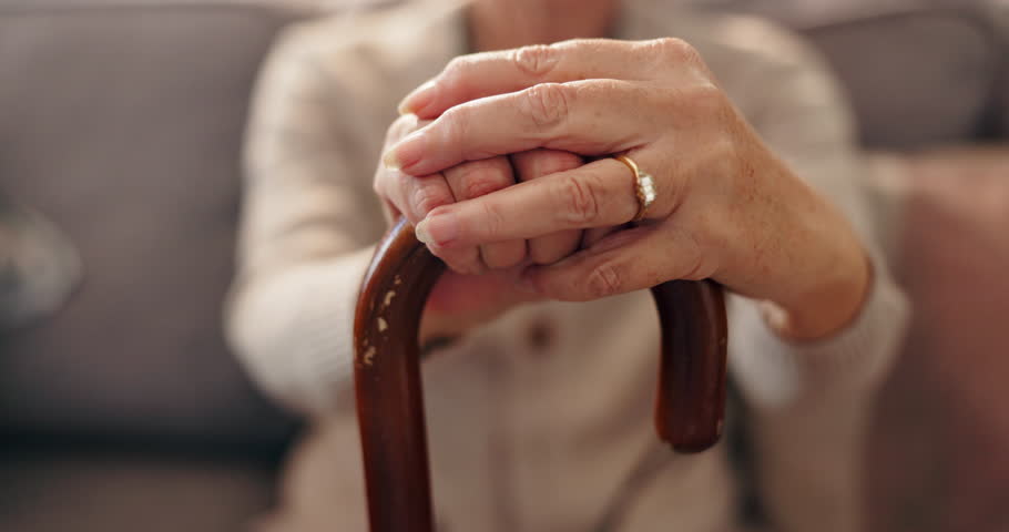 Senior woman, hands and cane in home for balance, support and retirement. Walking stick, elderly and person with disability in living room, osteoporosis and medical recovery for mobility with closeup