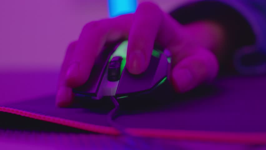 Close up of hand gripping gaming mouse on mouse pad, illuminated by vibrant purple and blue lighting, showcasing immersive gaming setup and advanced technology atmosphere.