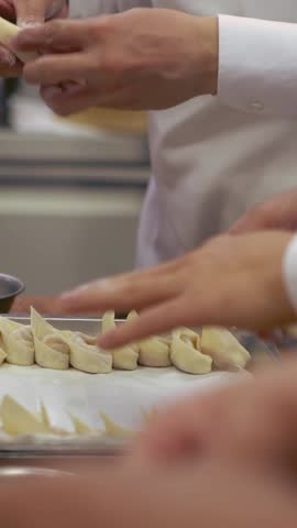 Vertical Taiwanese chefs in a kitchen deftly crafting fresh dumplings by hand. The process, rich in tradition, involves carefully preparing the dough, reflecting the culinary heritage of Taiwan.