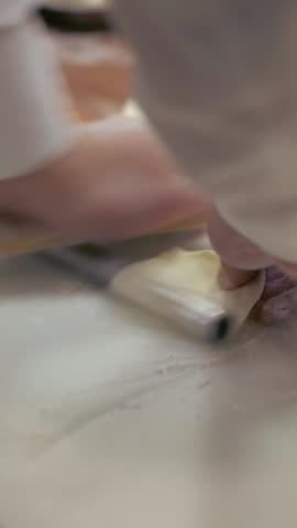 Vertical taiwanese chef rolls out dough before filling it with meat to create jiaozi, a Chinese dumpling. Asian man making fresh dumplings in a kitchen restaurant.