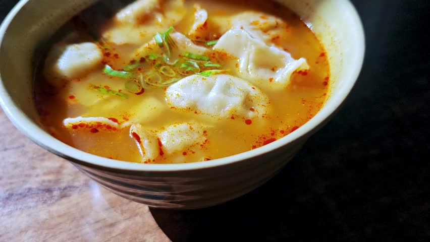 Thailand Tom Yum Soup (Tom Yum Goong) consisting of Chinese Dumplings (Wonton). Soup has curry flavoring and floating red chili oil. Catering concept. 4k60.