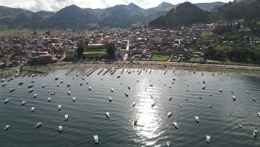 An aerial view of Copacabana Town with Titikaka Lake, boats, docks and mountains on a sunny day in Bolivia