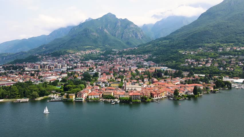 Aerial view of Mandello del Lario on Lake Como’s Lecco branch, with colorful houses, clear waters, and mountain backdrop. The home of Moto Guzzi, Birds Eye view harbor and alpine landscape.