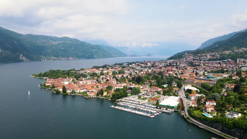 Aerial view of Mandello del Lario on Lake Como’s Lecco branch, with colorful houses, clear waters, and mountain backdrop. The home of Moto Guzzi, Birds Eye view harbor and alpine landscape.