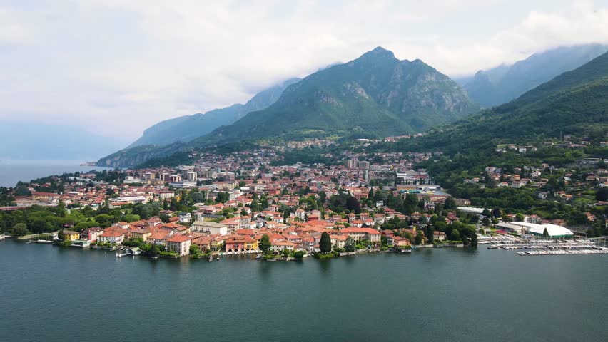 Aerial view of Mandello del Lario on Lake Como’s Lecco branch, with colorful houses, clear waters, and mountain backdrop. The home of Moto Guzzi, Birds Eye view harbor and alpine landscape.