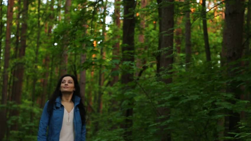 Beauty emotion woman walking on path in a green forest and relax spinning around. Cute girl hiking in wood and looking on trees on sunny summer day. Person coming in style fashion clothes