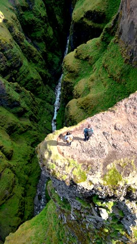 Aerial view reveals adventurers standing on the edge of a majestic canyon in Iceland, surrounded by vibrant green cliffs and a winding river below, Glymur waterfall canyon in Iceland
