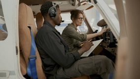 Caucasian female pilot pointing at cockpit controls and explaining instrument functions to Black male technician taking notes on clipboard during preflight aircraft check - Powered by Shutterstock - Get 15% off with code: PIKWIZARD15
