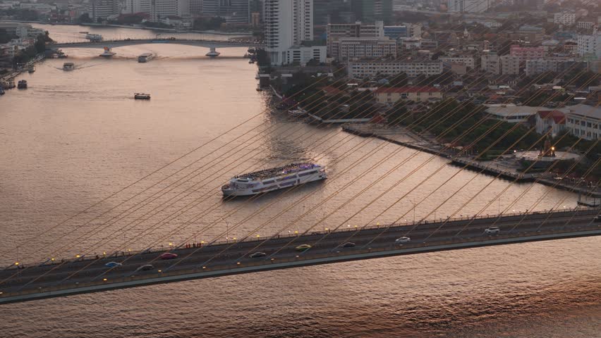 Passenger ferry crossing chao phraya river near rama viii bridge, bangkok skyline glowing during golden evening light, Thailand