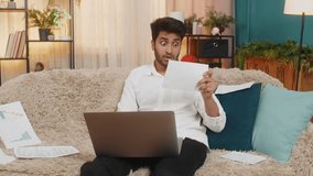 Indian man at home reviewing bills, calculating expenses, organizing personal finances while using a laptop. Arabian guy on sofa, focused on budget planning, making financial decisions thoughtfully - Powered by Shutterstock - Get 15% off with code: PIKWIZARD15
