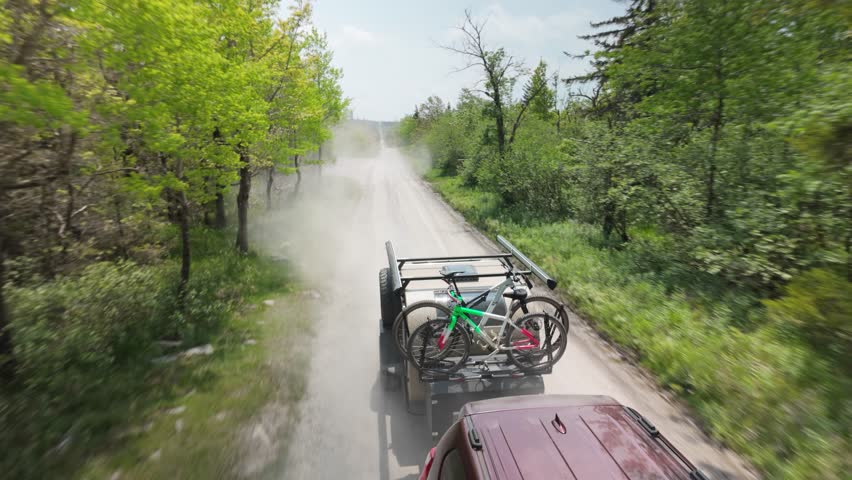 A teardrop camper trailer with bikes travels along a dusty road in Monongahela National Forest, surrounded by lush greenery and mountains during a peaceful camping trip.