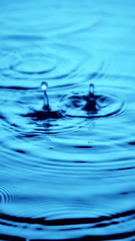 Vertical close up of rain drops falling into a puddle of water. Slow Motion.