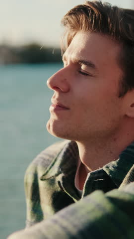 Vertical video, Young man enjoys the sunset over the Guadalquivir River in Seville. He takes a deep breath and smiles, feeling happy and relaxed in the golden light.