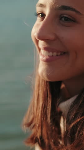 Vertical video, Young woman smiles and looks out over the Guadalquivir River in Seville at sunset. She's wearing a light sweater and enjoying the golden hour.